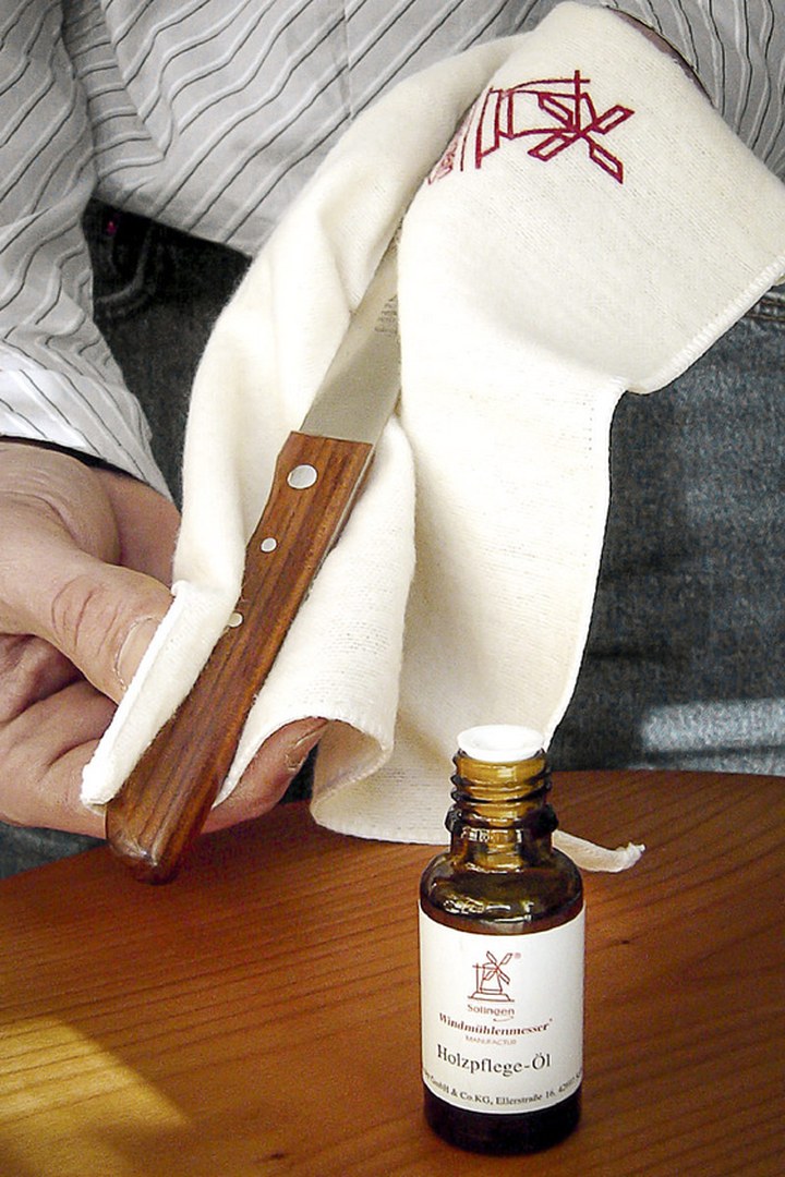 Wiping a Windmühlenmesser knife handle with a cloth next to a bottle of wood-care oil